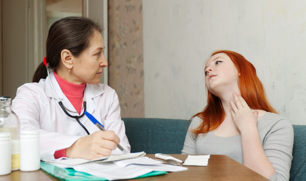 Speech-language pathologist consulting with an adult client who points to her throat during a swallowing or voice concern screening.