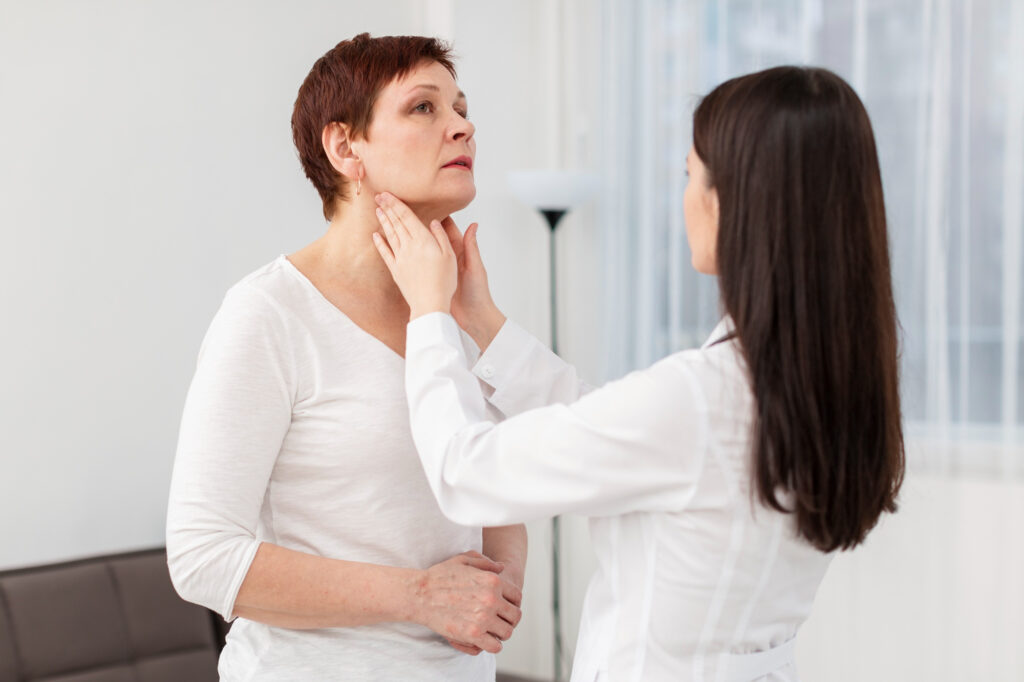 Speech-language pathologist gently assessing an adult woman’s neck and throat during a swallowing or voice evaluation in a clinic setting.
