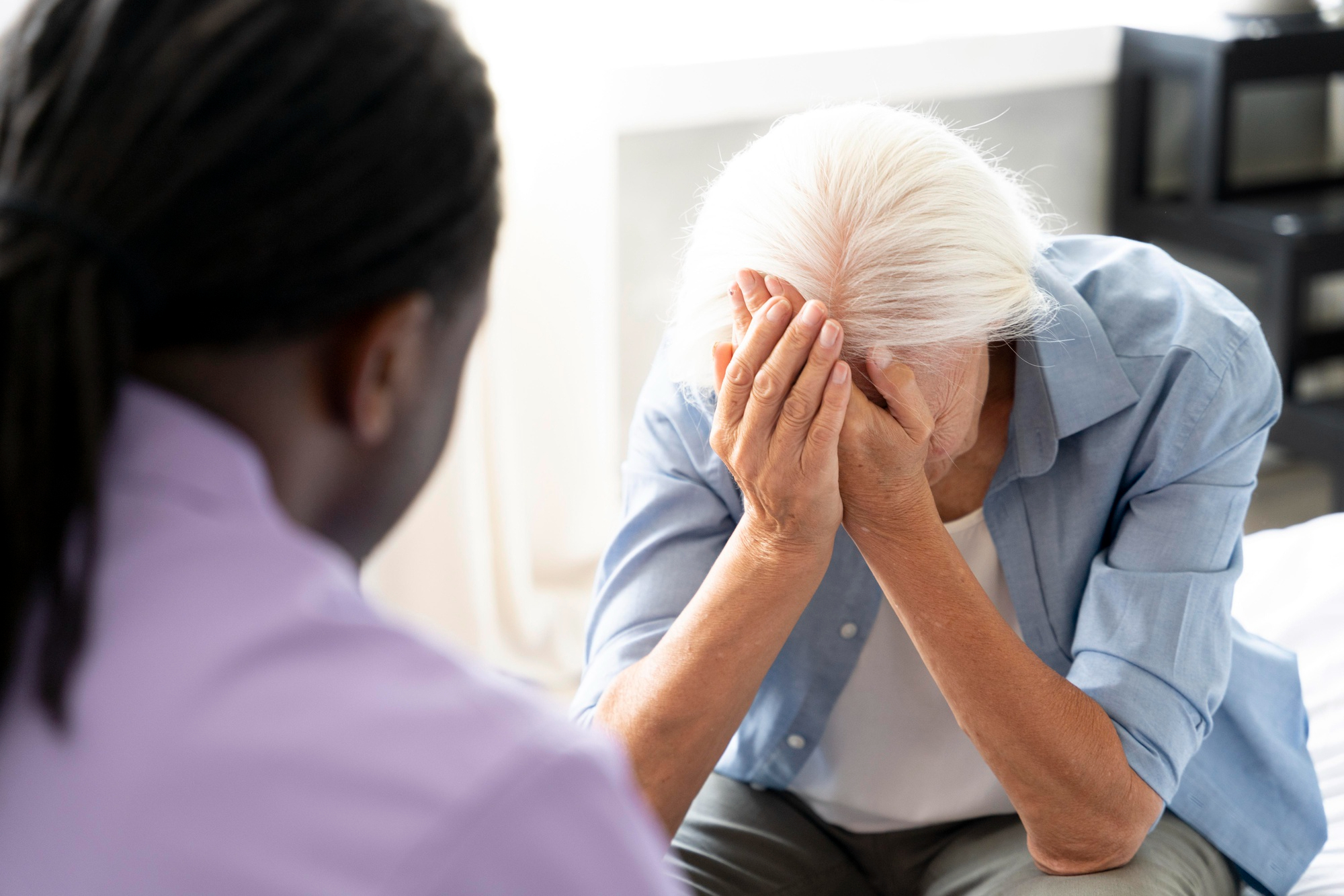 Older adult sitting with head in hands while speaking with a healthcare professional, showing stress or concern during a consultation.