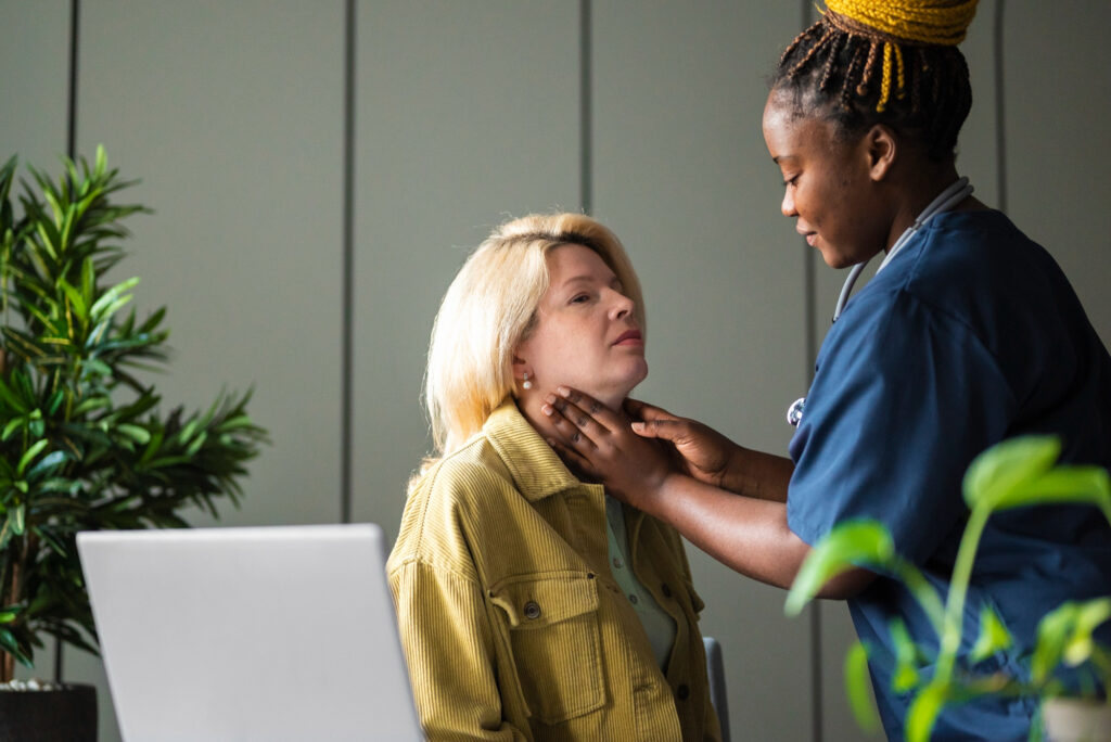 Healthcare clinician gently assessing an adult woman’s throat during a swallowing check in a clinic setting.